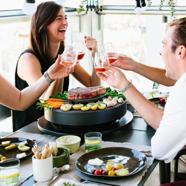 Grupo de amigos disfrutando de una comida alrededor de la barbacoa de mesa Tabl’O, cocinando carne y verduras.