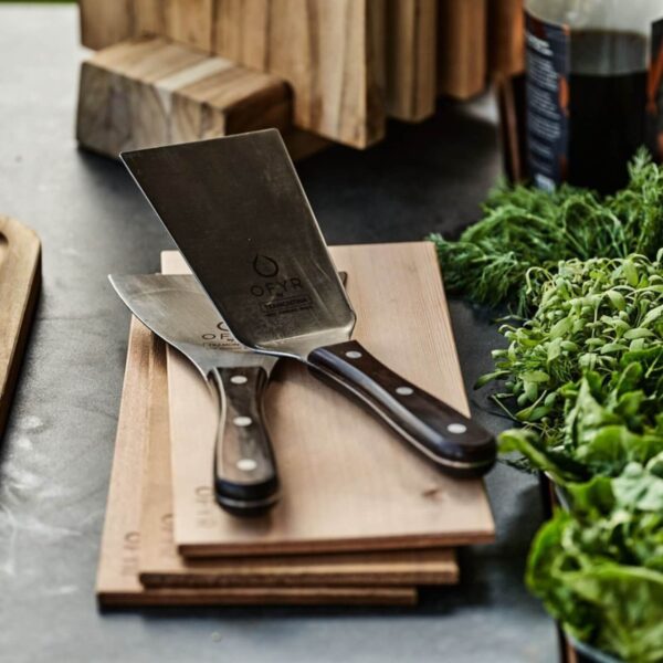 Set de espátulas OFYR con mangos de madera sobre una tabla de cocina, ideal para parrilladas y cocina al aire libre.