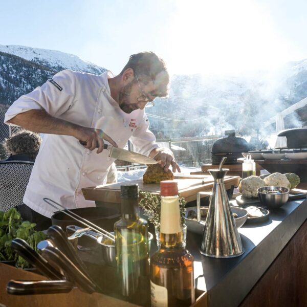 Chef cocinando al aire libre con la aceitera OFYR y diversos ingredientes en una montaña nevada