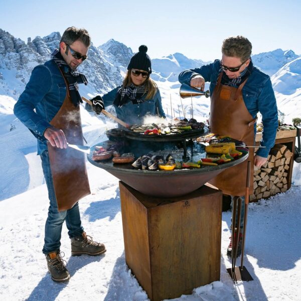 Grupo cocinando en una parrilla OFYR en la nieve, usando una aceitera OFYR para verter aceite