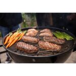 Varios filetes, zanahorias y espárragos cocinándose en la barbacoa de carbón Weber Master-Touch de 67 cm.