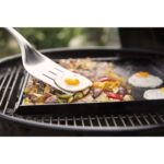 Huevos fritos y vegetales asados cocinándose en una plancha sobre la barbacoa de carbón Weber Master-Touch de 67 cm.