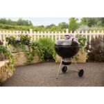 Barbacoa de carbón Weber Master-Touch de 67 cm ubicada en un patio con jardín y flores alrededor.
