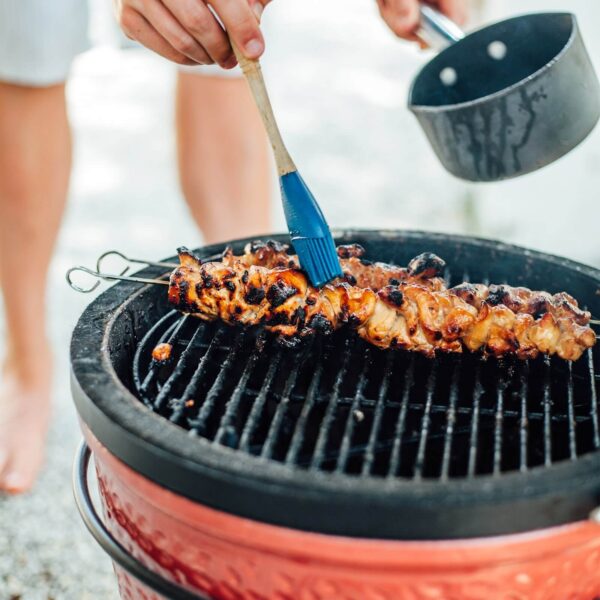 Persona aplicando salsa a brochetas de carne asada sobre una parrilla Kamado Joe Jr.