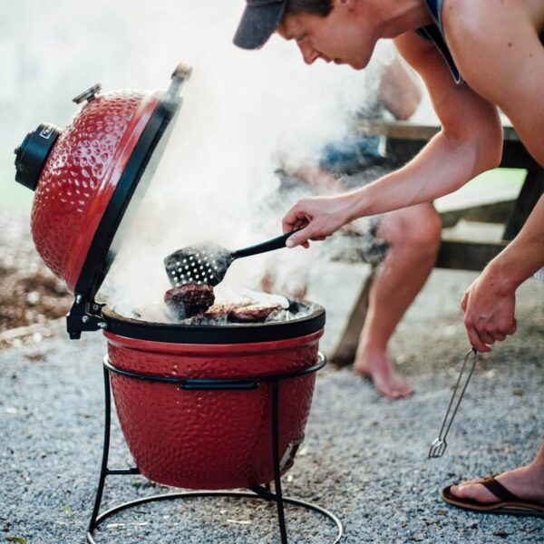 Persona cocinando hamburguesas en el Kamado Joe Jr. en un entorno al aire libre.