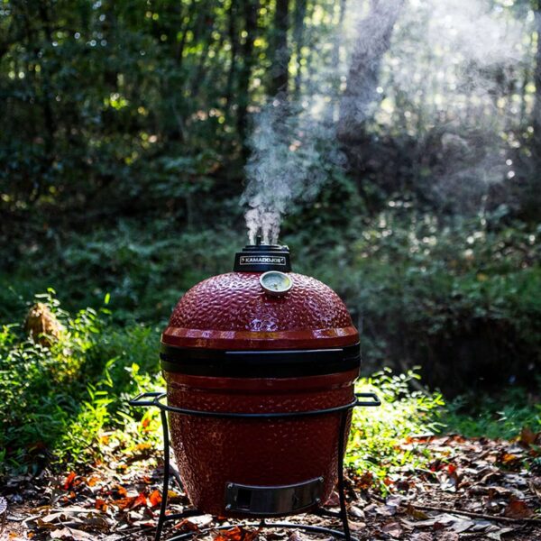 Kamado Joe Jr. emitiendo humo mientras se cocina en un entorno de bosque.