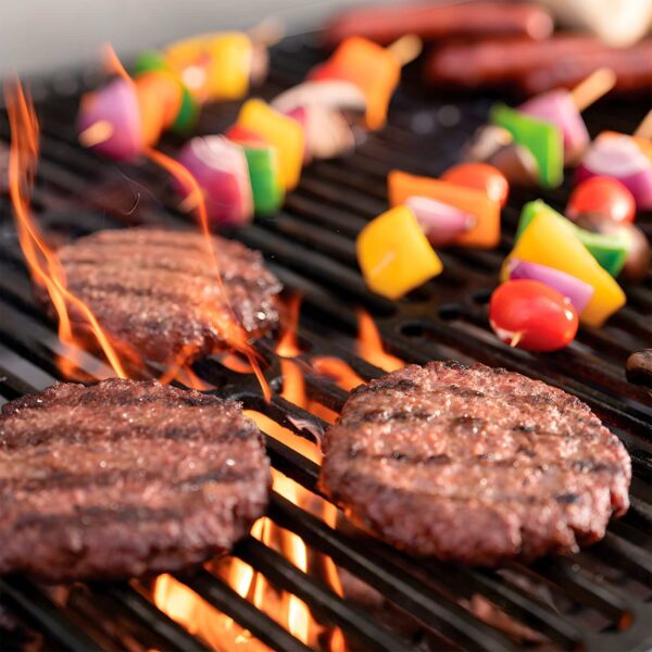 Hamburguesas y brochetas de vegetales cocinándose sobre llamas en la Barbacoa de Carbón Wrangler de Char-Griller.