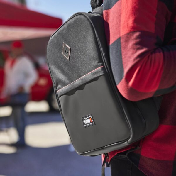 Persona usando la Mochila Porta Utensilios Weber negra, ideal para transportar herramientas de barbacoa en actividades al aire libre.