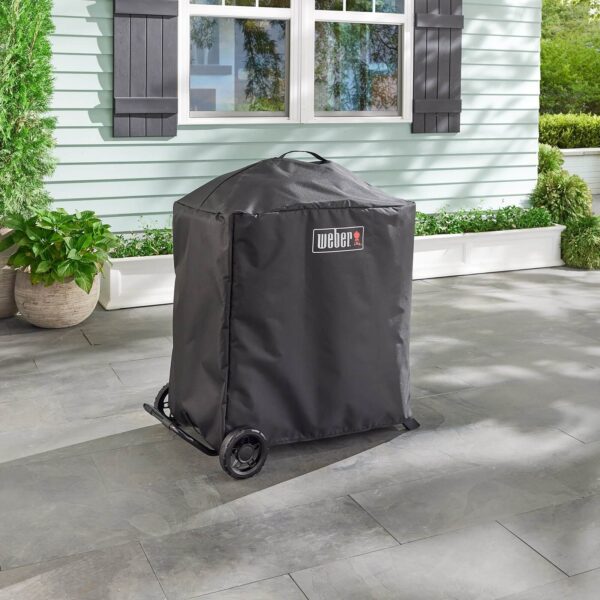 Funda negra resistente para barbacoa Weber Traveler Compact con carrito, ubicada en un patio exterior.