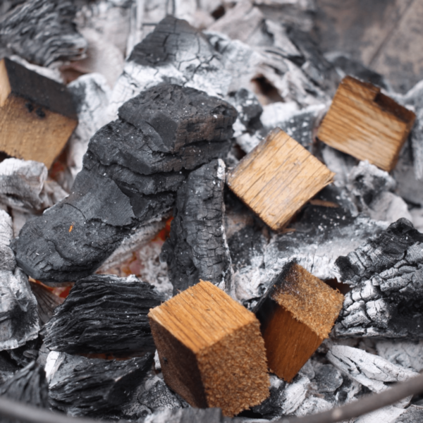 Chunks de madera de Cook in Wood sobre brasas ardientes para ahumado prolongado en BBQ.