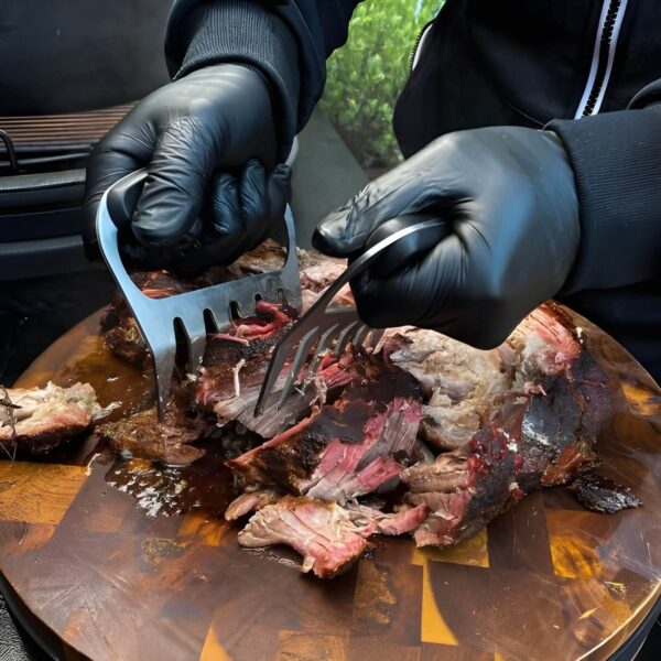 Persona desmenuzando carne asada con las garras Killer Claws de The Bastard en una tabla de madera.