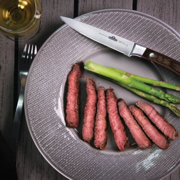 Plato gourmet con filetes de carne cortados finamente al lado de espárragos verdes, con un cuchillo de carne profesional de Napoleon y una copa de vino blanco.