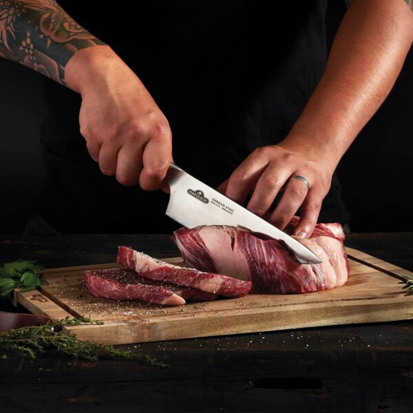 Persona cortando un trozo de carne cruda con el Cuchillo Chef Napoleon sobre una tabla de madera, con hierbas frescas al costado.