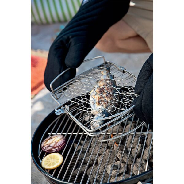 Manos con guantes de cocina manejando una Cesta para Asar Weber, cocinando un pescado entero en una parrilla de carbón.