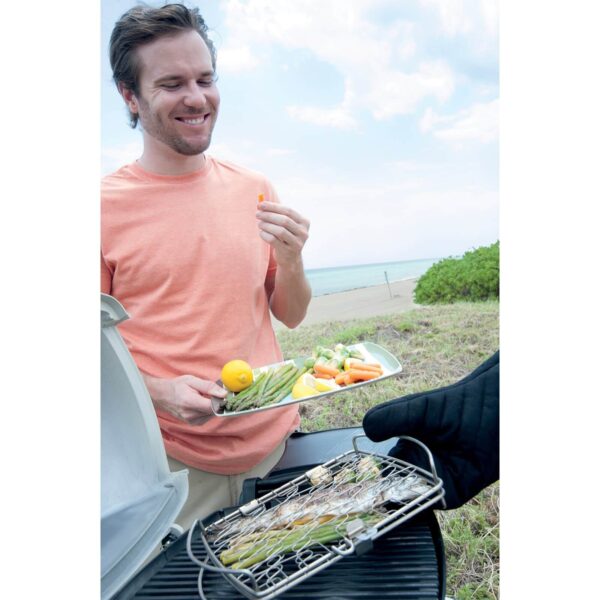 Hombre disfrutando de una parrillada al aire libre con la Cesta para Asar Weber, cocinando pescado y verduras.