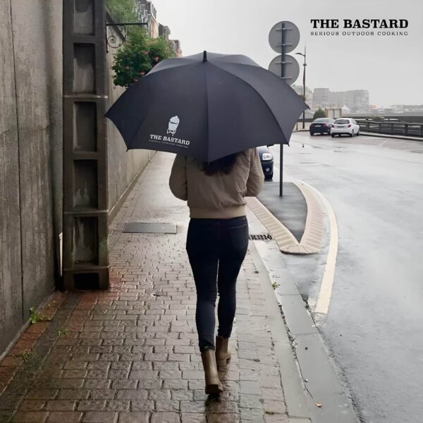 Persona caminando bajo la lluvia con el paraguas The Bastard negro, mostrando su amplio tamaño y diseño elegante.