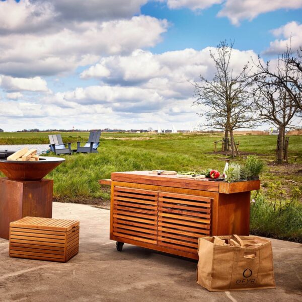 Bolso para madera OFYR de jute colocado junto a una estación de cocina al aire libre con parrilla y muebles de madera.