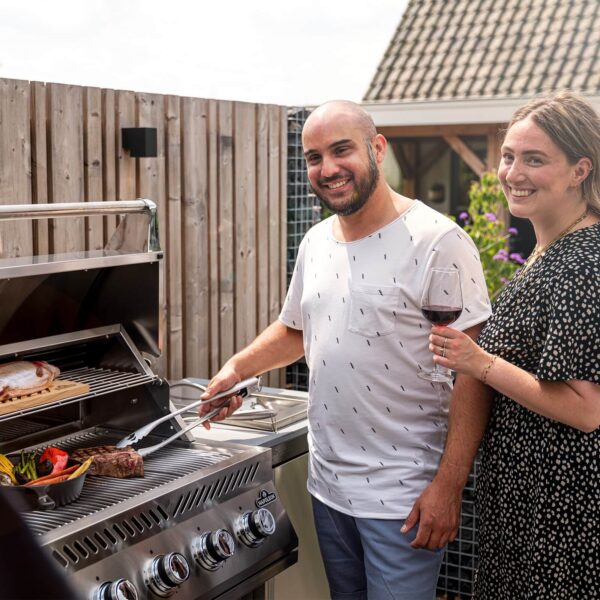 Pareja sonriente cocinando en la barbacoa Napoleon Serie 500 32 mientras disfrutan de una copa de vino.