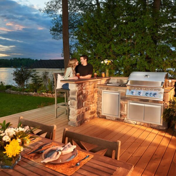 Pareja disfrutando de una cocina al aire libre con la Barbacoa de Gas Serie 700 32 RB de Napoleon al atardecer junto a un lago.