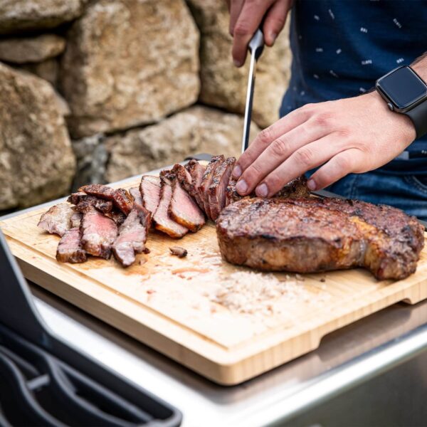 Persona cortando carne asada con el Cuchillo Chef Napoleon sobre una tabla de madera al aire libre.