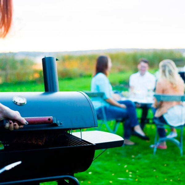 Barbacoa Black Taurus 660+ en primer plano con un grupo de amigos disfrutando de un encuentro social al aire libre en el fondo.