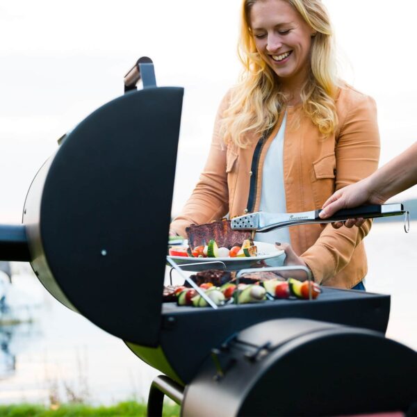 Una mujer sonriente usando la barbacoa Black Taurus 660+ para asar carnes y vegetales, destacando la facilidad de uso y la calidad de cocción.