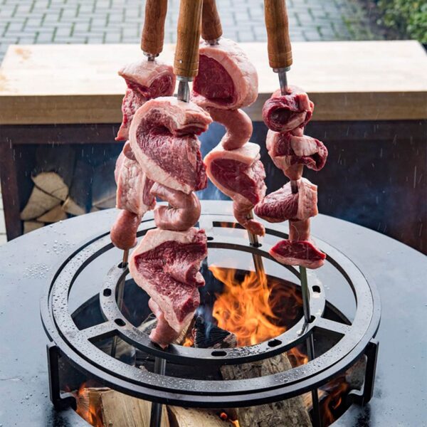 Brochetas de carne cruda cocinándose en un anillo para parrilla brasileña sobre fuego de leña