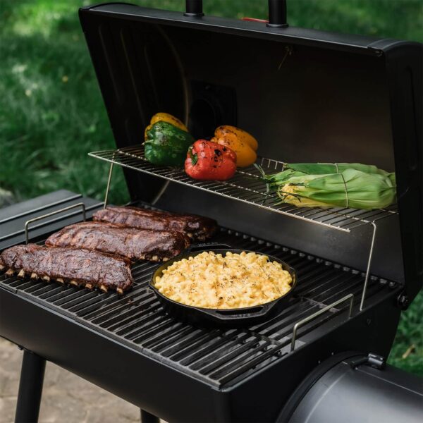 Costillas, macarrones con queso, pimientos asados y mazorcas cocinándose en una barbacoa con tapa abierta.