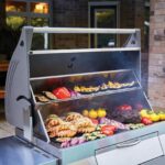 Barbacoa de Carbón Profesional Napoleon con tapa abierta mostrando alimentos asándose.