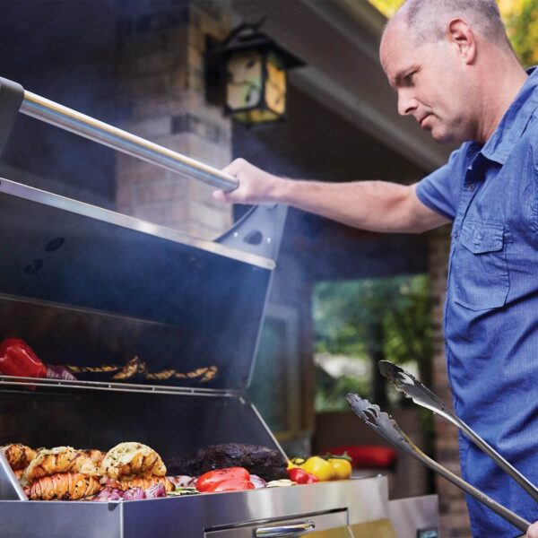 Hombre cocinando en la Barbacoa de Carbón Profesional Napoleon con alimentos variados en la parrilla.