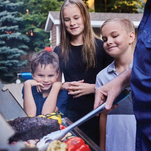 Tres niños observando la comida cocinándose en la Barbacoa de Carbón Profesional Napoleon.