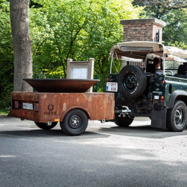 Vehículo todoterreno remolcando una barbacoa de leña montada sobre un trailer de acero corten, listo para ser transportado a un evento.