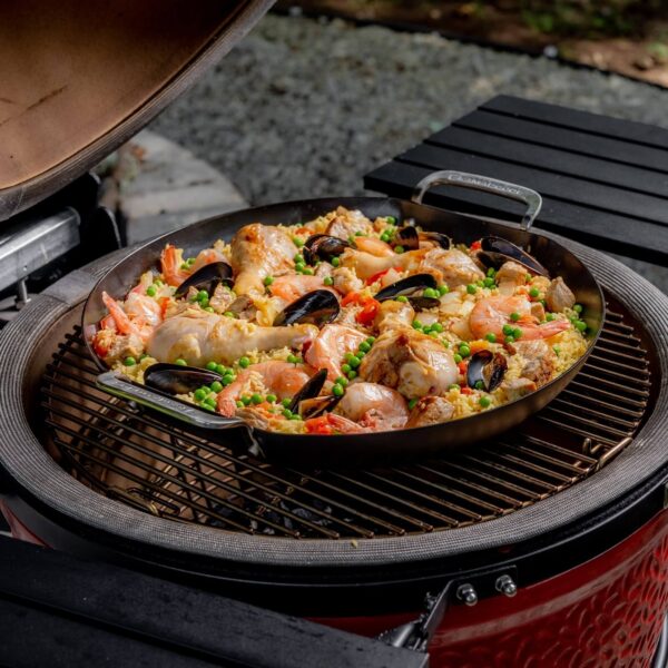 Paella de mariscos y pollo en una paellera Kamado Joe sobre una parrilla kamado con la tapa abierta.