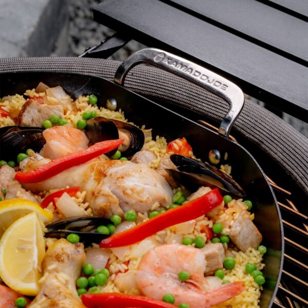 Primer plano del asa de acero inoxidable de la paellera Kamado Joe con paella de mariscos y pollo.