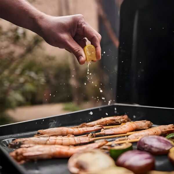 Mano exprimiendo un limón sobre camarones y vegetales en la Plancha Weber SLATE GP 43 cm Premium.