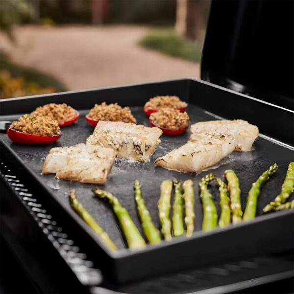 Plancha Weber SLATE GP 56 cm Premium cocinando filetes de pescado, pimientos rellenos y espárragos en un ambiente al aire libre.