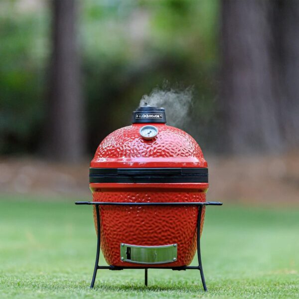 Kamado Joe Jr. emitiendo humo mientras se cocina en un entorno de jardín.