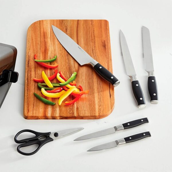 Conjunto de cuchillos de cocina Ninja sobre una tabla de cortar de madera. Hay un cuchillo de chef junto a pimientos de diferentes colores, y a un lado están un cuchillo para pan, un cuchillo para rebanar, tijeras y otros dos cuchillos más pequeños.