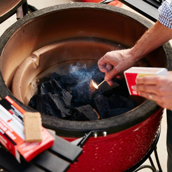 Hombre encendiendo carbón en una parrilla Kamado Joe con un fósforo.