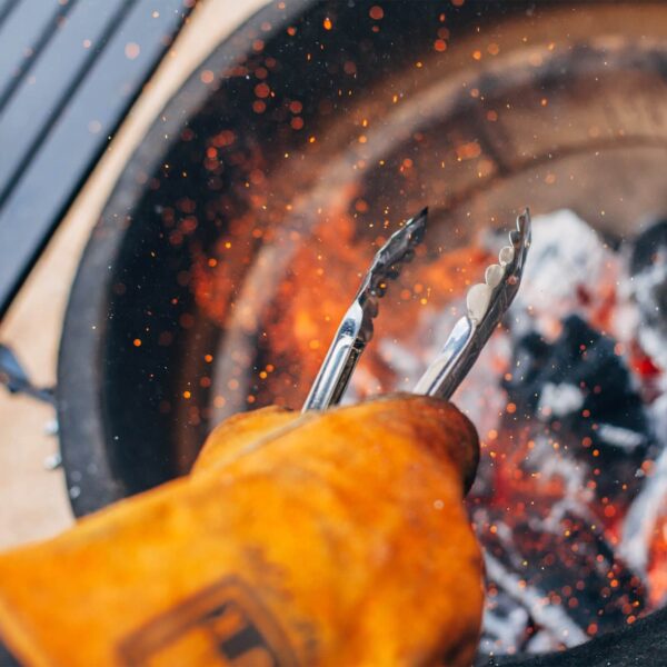 Tenazas ajustando brasas encendidas en una parrilla Kamado Joe.