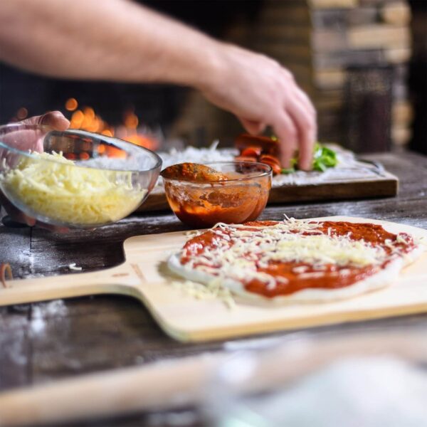 Pala de pizza de madera Kamado Joe utilizada para preparar y servir pizza en una parrilla Kamado Joe.