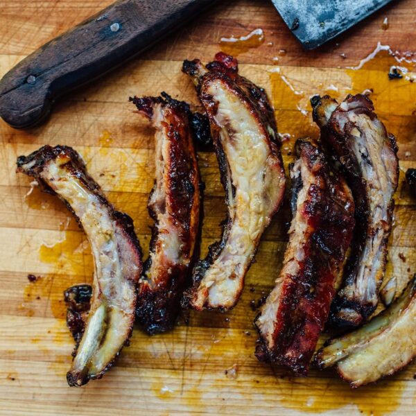 Costillas asadas y jugosas recién cortadas sobre una tabla de madera junto a un cuchillo de cocina.