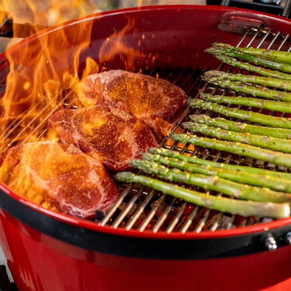 Carne y espárragos cocinándose en la parrilla de la Kamado Kettle Joe con llamas intensas.