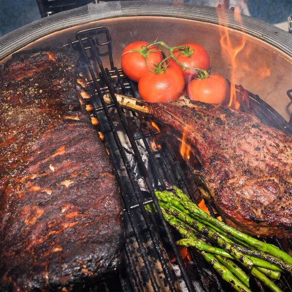 Costillas, tomahawk, espárragos y tomates asándose en la parrilla del Kamado Big Joe III.