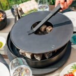 Colocación de la tapa en la parrilla OFYR Tabl'O con briquetas de coco encendidas, lista para cocinar.