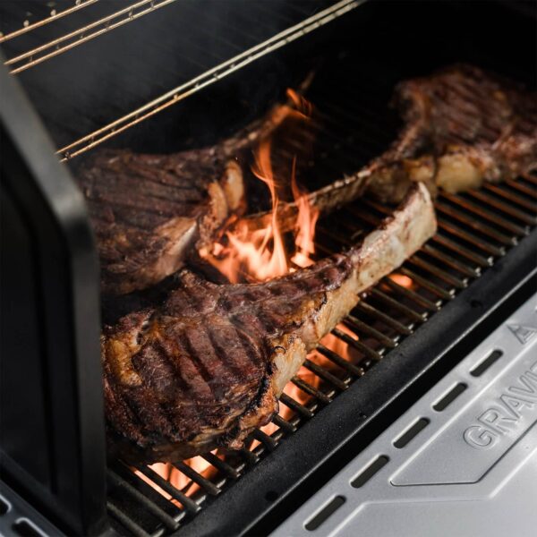 Costillas cocinándose sobre las rejillas de la Barbacoa Gravity Series XT de Masterbuilt, con llamas visibles entre la carne.