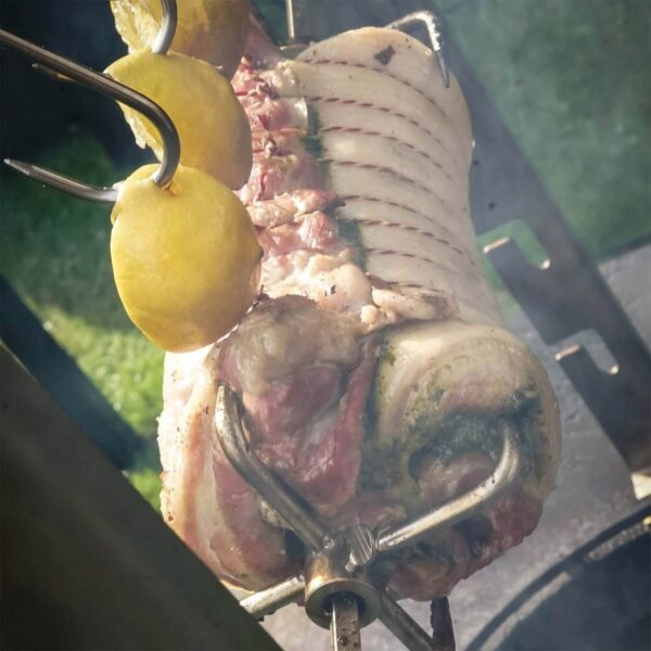 Panceta de cerdo Duroc rellena de pesto cocinándose en asador con rodajas de limón.