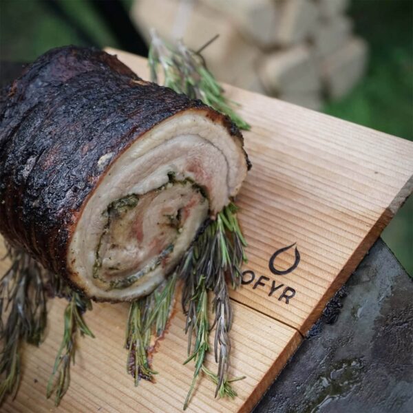 Panceta de cerdo Duroc rellena de pesto casero servida sobre una tabla de madera con ramas de romero.