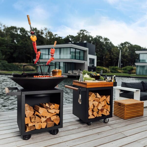 Asador con anillo para parrilla, brochetas de verduras y mesa de preparación con almacenamiento de leña en un muelle junto al lago