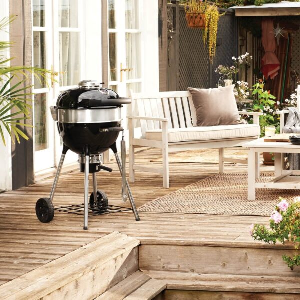 Barbacoa Pro Kettle 47 cm 2024 de Napoleon en una terraza de madera, complementando un espacio exterior acogedor con mobiliario blanco.